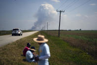 Farmworkers and allies pause for a lunch break, as smoke reportedly from a burning sugar cane field, rises in the background on the first day of a five-day trek aimed at highlighting the Fair Food Program, which has enlisted food retailers to use their clout with growers to ensure better working conditions and wages for farmworkers, Tuesday, March 14, 2023, in Pahokee, Fla. (AP Photo/Rebecca Blackwell)