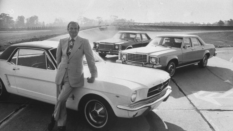 Lee Iacocca posing with a Ford Mustang and other vintage cars