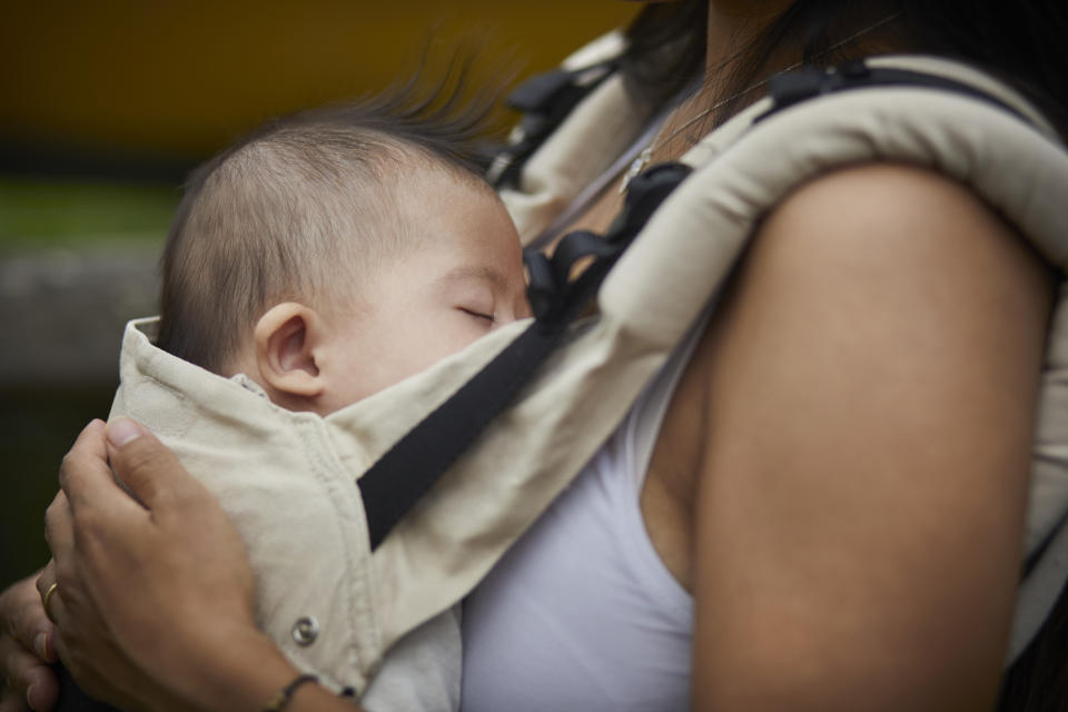 Baby sleeping in a carrier against a person's chest, showing close bonding