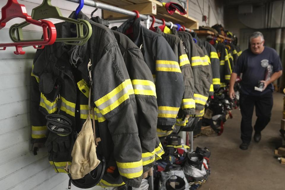 A firefighter walks past a row of firefighter equipment.