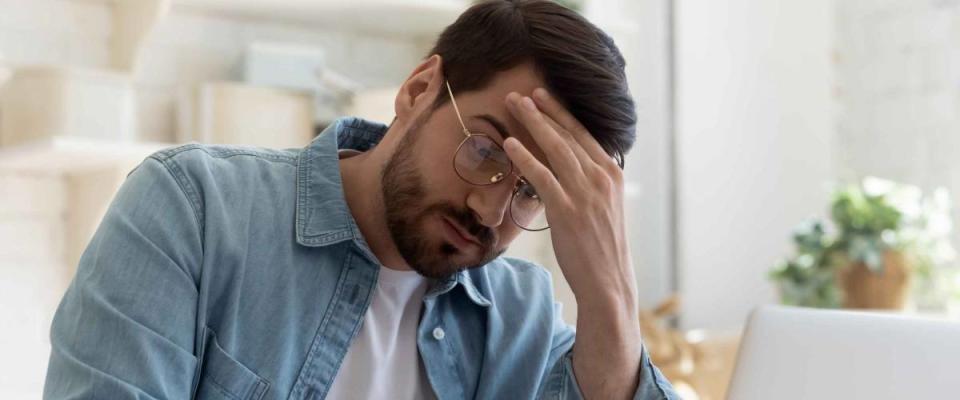 Man holds head in hand, looking down while sitting at a desk