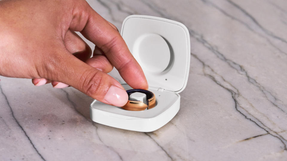 The Evie smart ring in its charging case, with a woman's hand reaching to pick it up.