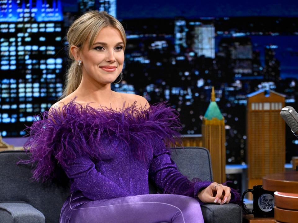 Millie Bobby Brown in a purple outfit with feathers during a late-night interview