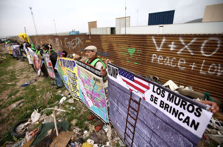 People hold signs during a protest while standing in front of the current border fence and near the prototypes of U.S. President Donald Trump's border wall, in Tijuana, Mexico March 13, 2018. REUTERS/Edgard Garrido