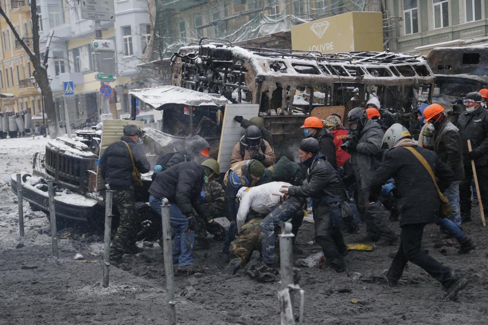 Protesters try to help their wounded comrade, center, during clashes with police in central Kiev, Ukraine, early Wednesday, Jan. 22, 2014. Two people have died in clashes between protesters and police in the Ukrainian capital Wednesday, according to medics on the site, in a development that will likely escalate Ukraine’s two month-long political crisis. (AP Photo/Sergei Grits)