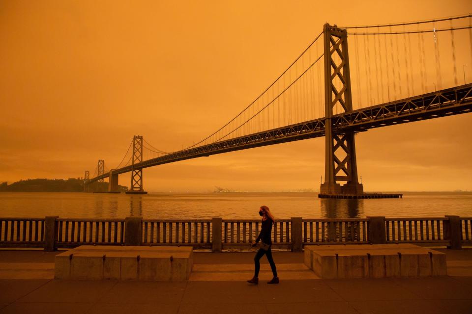 TA woman walks along The Embarcadero under an orange smoke-filled sky in San Francisco, California on September 9, 2020.  / Credit: BRITTANY HOSEA-SMALL/AFP via Getty Images