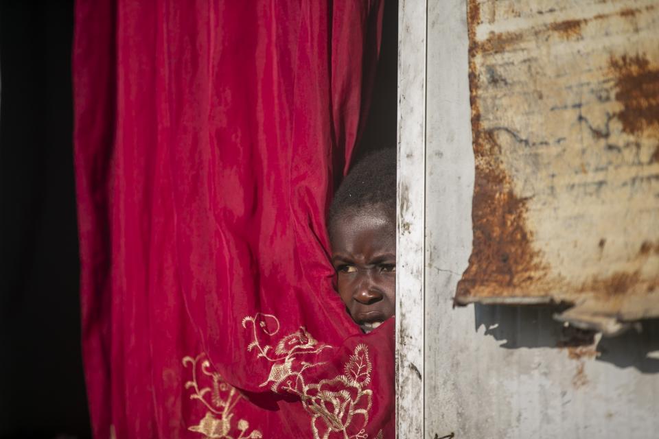 Jonelson Princeton, 7, who survived cholera as a newborn, peers out from inside his home which was once used as an office, on a former UN base where he lives with his parents and grandmother in Mirebalais, Haiti, Monday, Oct. 19, 2020. Ten years after a cholera epidemic swept through Haiti and killed thousands, families of victims still struggle financially and await compensation from the United Nations as many continue to drink from and bathe in a river that became ground zero for the waterborne disease. (AP Photo/Dieu Nalio Chery)