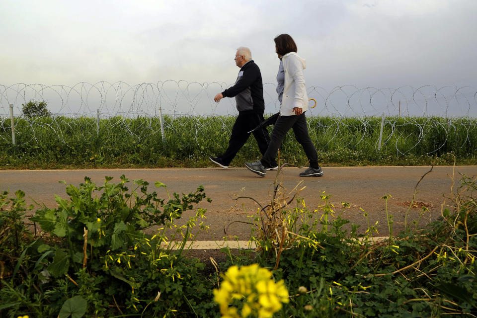 A couple walk along a row of razor wire along the southern side of a U.N buffer zone that cuts across the ethnically divided Cyprus, during sunset near village of Astromeritis, Tuesday, March 9, 2021. The government of ethnically split Cyprus has come under fire over a decision to lay razor wire along a section of a U.N. controlled buffer zone it said is needed to stem migrant inflows from the island's breakaway north, with critics charging that the "ineffective" scheme only feeds partitionist perceptions amid a renewed push resume dormant peace talks. (AP Photo/Petros Karadjias)