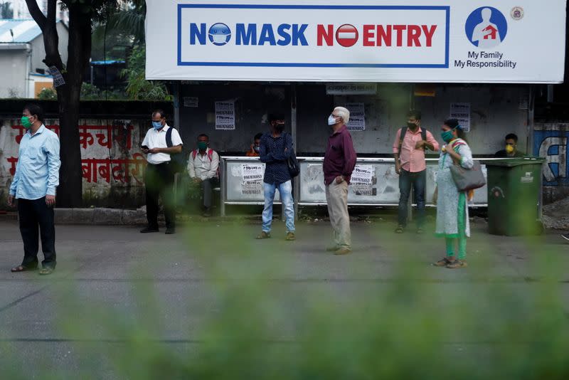 People wearing protective masks wait at a bus stop amidst the spread of the coronavirus disease (COVID-19), in Mumbai