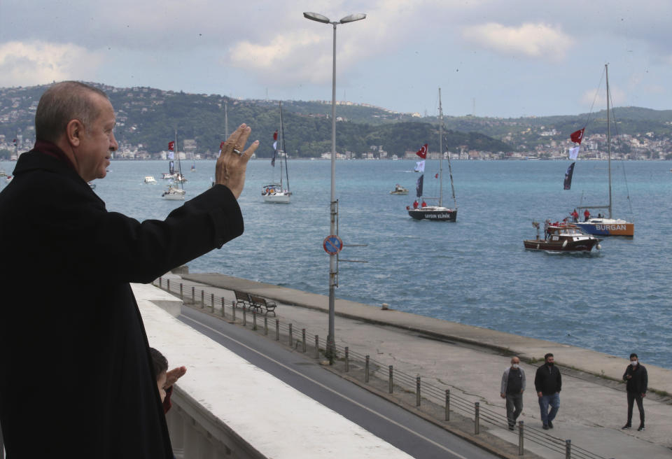 Turkey's President Recep Tayyip Erdogan salutes vessels decorated with Turkish flags as they sail the Bosporus Strait in Istanbul, part of the celebrations for the 567th anniversary of the Ottoman conquest of the city, then known as Constantinople, in 1453, on Friday, May 29, 2020. (Presidential Press Service via AP, Pool)