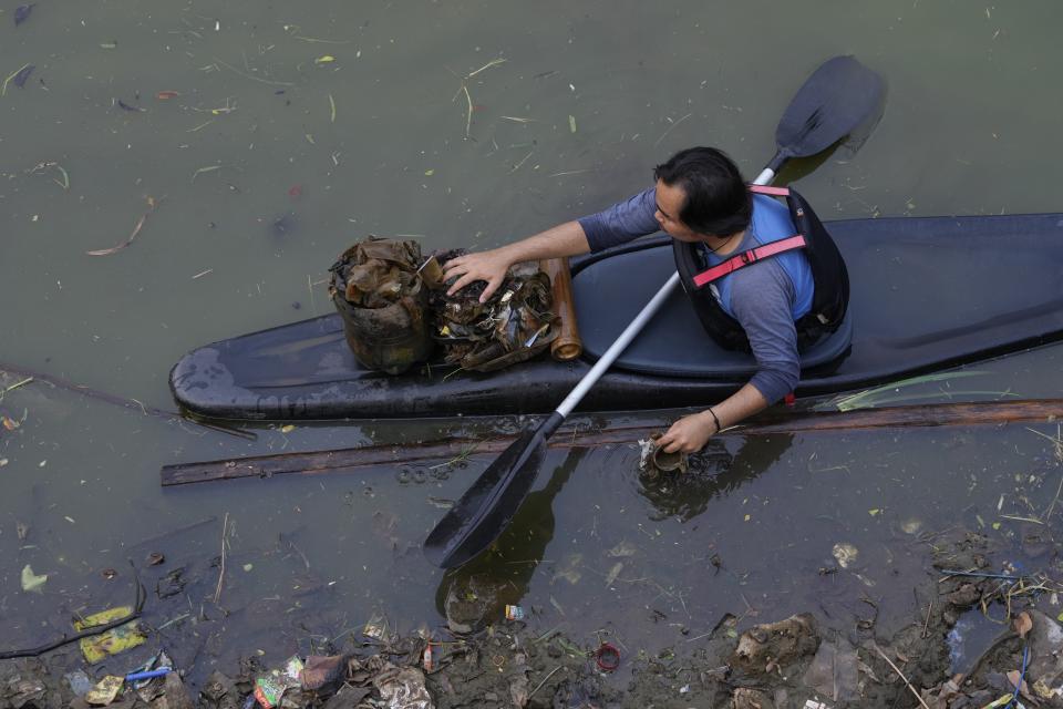 An environmental activist of Situ Gede Cleanliness Warrior picks up trash while paddling a kayak at Setu Gede lake in Bogor, West Java, Indonesia, Tuesday, Oct. 10, 2023. Young people have been at the forefront of environmental and climate change movements in the recent years: initiatives like school strikes for climate action, protests at United Nations climate talks and around the world and local clean ups have often been youth-led.(AP Photo/Achmad Ibrahim)