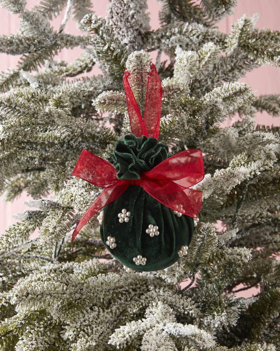 green velvet wrapped ornament with red bow and white mini pearl beads hanging on a tree