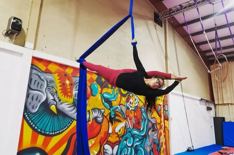 A member of the circus group doing an aerial skill in front of the mural, which includes colourful depictions of people, lions and tigers on an orange, yellow and blue background