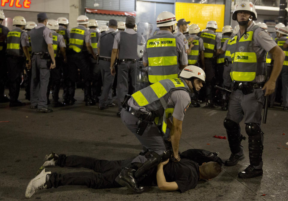 Policemen detain a demonstrator during a protest against the upcoming World Cup soccer tournament, in Sao Paulo, Brazil, Saturday, Feb. 22, 2014. Hundreds of protesters gathered demonstrating against the billions of dollars being spent to host this year's World Cup while the nation's public services remain in a woeful state. The protest started peacefully, but adherents to the Black Block anarchist tactics vandalized banks and clashed with police, who used tear gas and stun grenades to disperse the violent demonstrators. (AP Photo/Andre Penner)