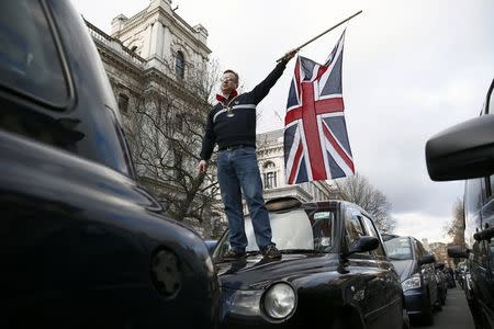 A London cab driver waves a Union flag as he stands on the bonnet of his taxi during a protest against Uber on Whitehall in central London, February 10, 2015 REUTERS/Stefan Wermuth