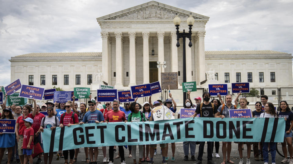 Environmental activists rally in front of the U.S. Supreme Court holding a banner saying: Get Climate Done, as well as placards saying things like: People v. Polluters, Climate Action Now and Congress:#Climatecantwait.  