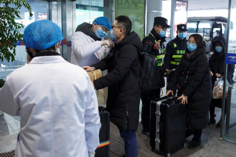 Un agente sanitario toma la temperatura corporal de un hombre en la sala de salida del aeropuerto de Changsha, provincia de Hunan, China, el 27 de enero de 2020