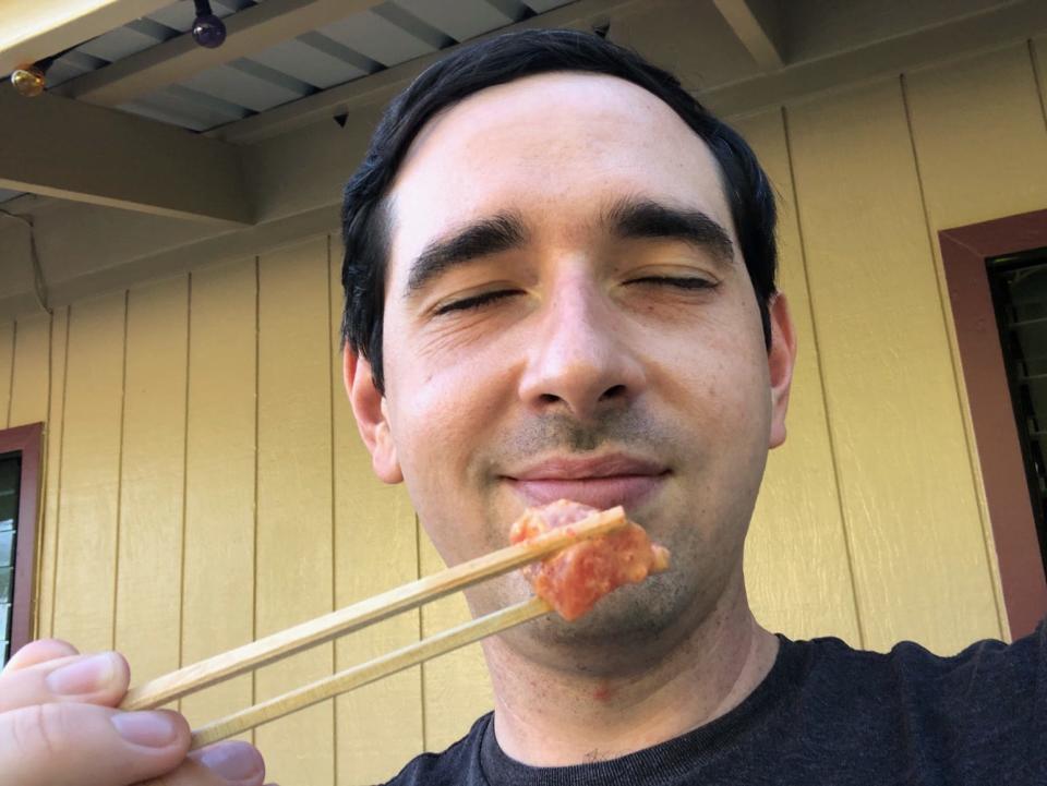 Reporter Alex Bitter smiles and holds a piece of spicy ahi poke using chopsticks