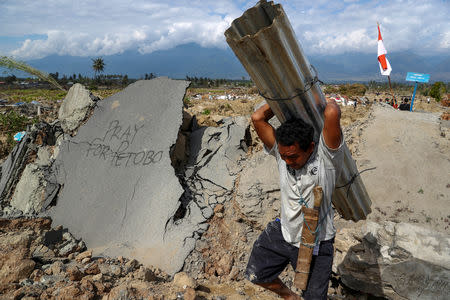 A villager carries zinc roof, as he walks past an area after an earthquake hit Petobo neighbourhood in Palu, Indonesia, October 6, 2018. REUTERS/Athit Perawongmetha