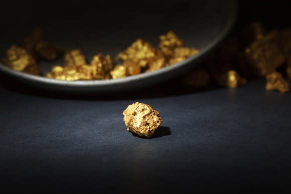 Gold nugget on table next to pan used to search for gold.