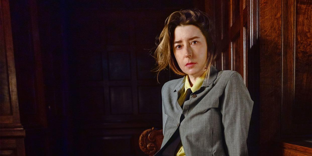 portrait of alexandra cunningham cameron in a suit legs crossed and sitting on a pew like bench