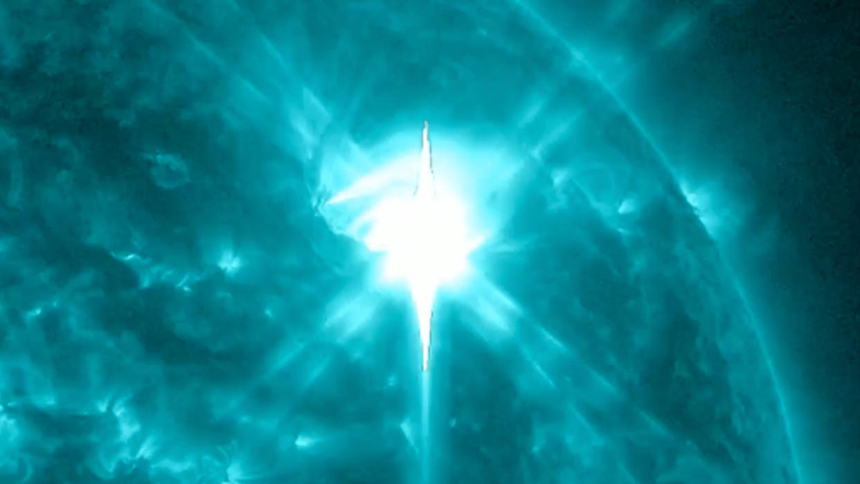  In a colorized view of the sun, a large bright spot emerges against a field of swirling green. 