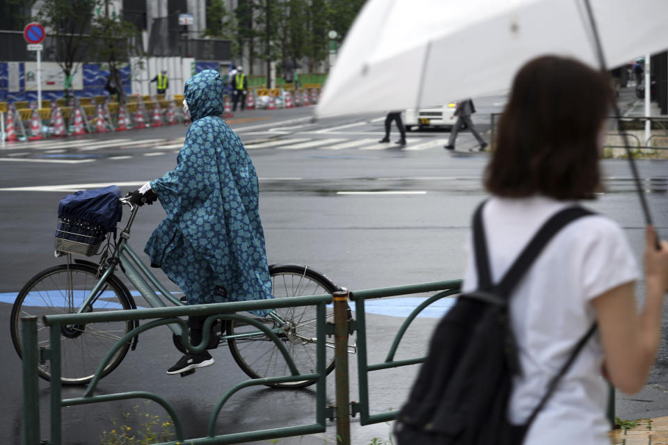 A woman wearing a protective mask to help curb the spread of the coronavirus rides a bicycle in the rain Monday, June 14, 2021, in Tokyo. Japan is desperately pushing to accelerate the pace of inoculations before the Tokyo Olympics. (AP Photo/Eugene Hoshiko)