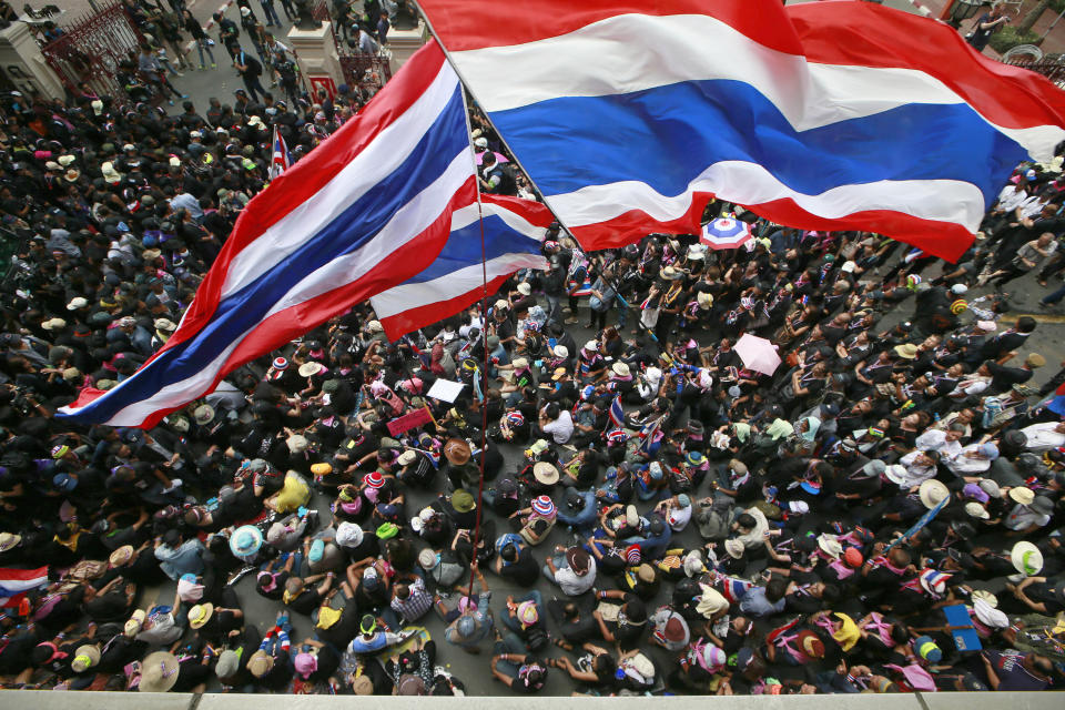 Anti-government protesters wave national flags at the gates of the police headquarters during a memorial for the children killed in recent bomb blasts in Bangkok, Thailand, Wednesday, Feb. 26, 2014. Violence spread Tuesday to another anti-government protest site in Thailand's capital following weekend explosions that left five people dead, including four children, security officials said. (AP Photo/Wason Wanichakorn)