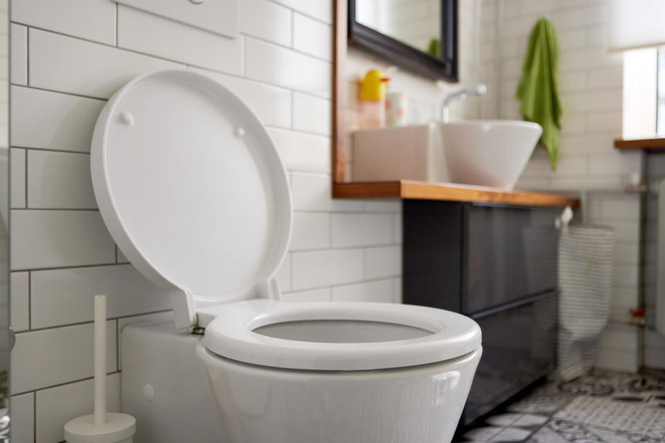 A clean, white toilet with the lid up in a tiled bathroom with sink and towel visible