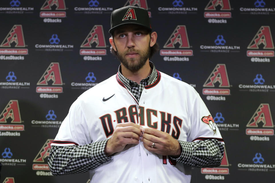 FILE - In this Dec. 17, 2019, file photo, newly acquired Arizona Diamondbacks pitcher Madison Bumgarner puts on a jersey after being introduced during a team availability in Phoenix. The Diamondbacks added a handful of veteran free agents during the offseason, including Bumgarner, outfielder Kole Calhoun, catcher Stephen Vogt and reliever Héctor Rondón. The left-handed Bumgarner — a four-time All-Star and 2014 World Series MVP — was the marquee signing, joining the rotation on an $85 million, five-year deal. (AP Photo/Matt York, File)