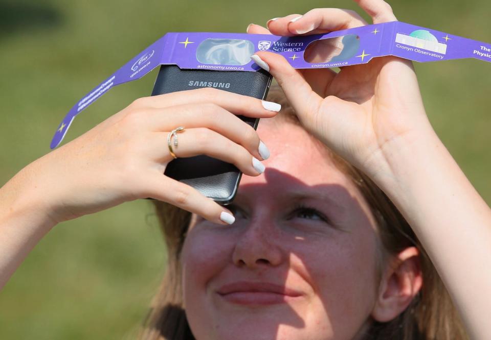Mélanie Meinrad uses solar glasses to take a photo of the eclipse with her phone. Hundreds of people gathered at Western University to view the partial solar eclipse, in London, Ont. on Aug. 21, 2017.