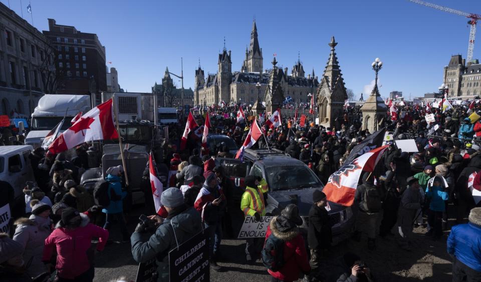 People waving Canada's red and white flag gather around vehicles outside a building