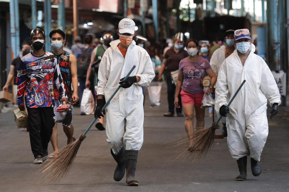 Workers wearing protective suits walks beside residents at a public market during the start of a stricter lockdown to help prevent the spread of the coronavirus in Marikina city, Philippines on Monday, March 29, 2021. Philippine officials placed Metropolitan Manila and four outlying provinces, a region of more than 25 million people, back to a lockdown Monday at the height of the Lenten and Easter holiday travel season as they scrambled to control an alarming surge in coronavirus infections. The Department of Health reported more than 10,000 new COVID-19 cases Monday, the highest since the pandemic hit the country. (AP Photo/Aaron Favila)