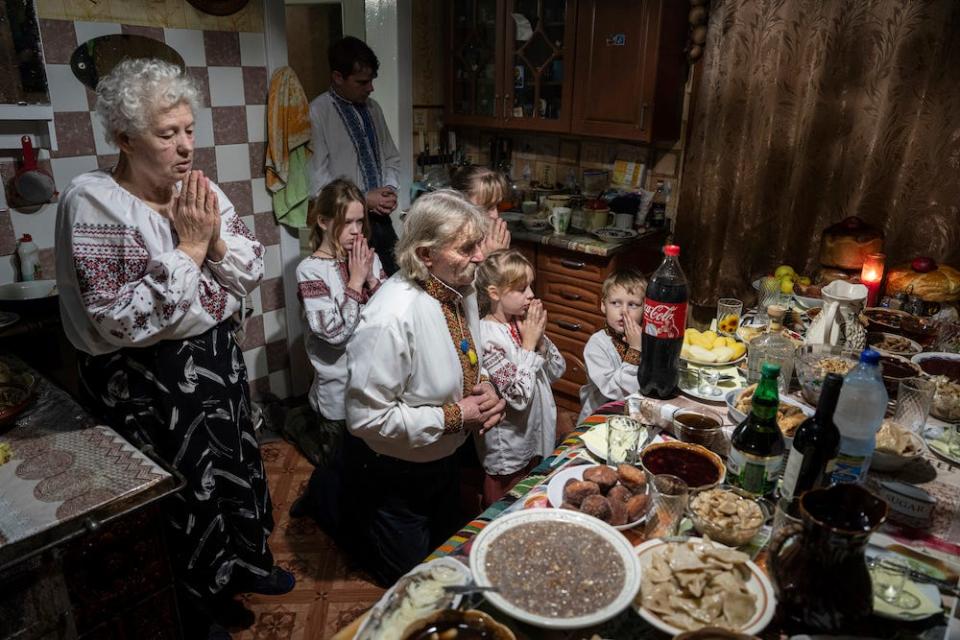 The Zelenchuk family — two elderly people, an adult, and four children — prays in front of a table laden with food — in Kryvorivnia village, Ukraine, Sunday, Dec. 24, 2023