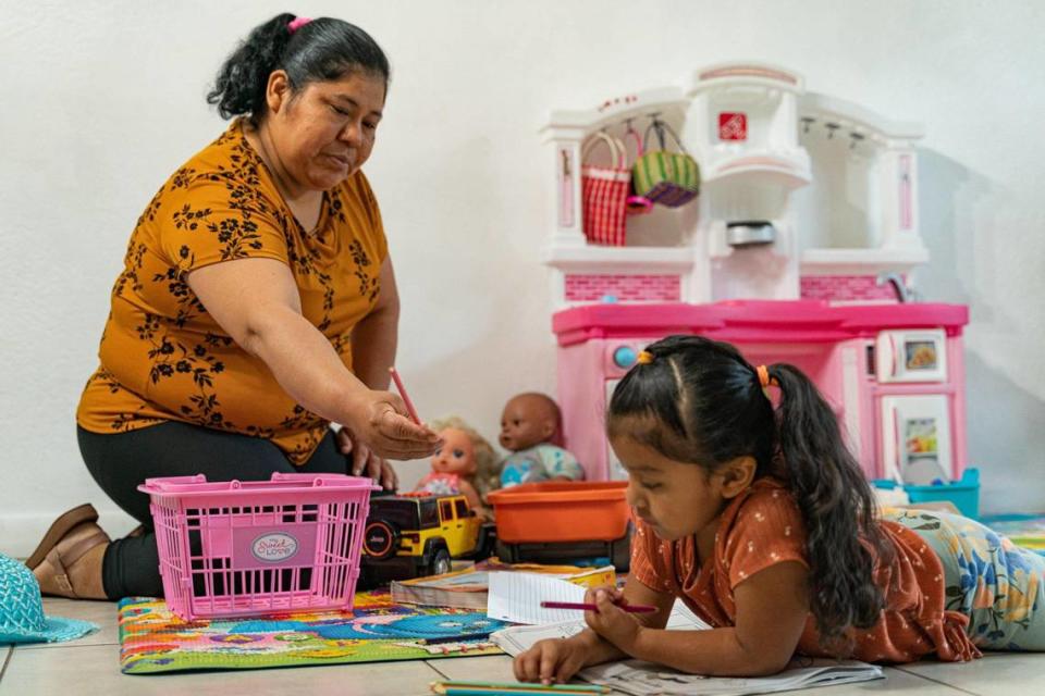 Alida Tomás Méndez entrega un lápiz de color a su hija Yaily Mejía en su casa de Homestead, Florida, el lunes 21 de noviembre de 2022.