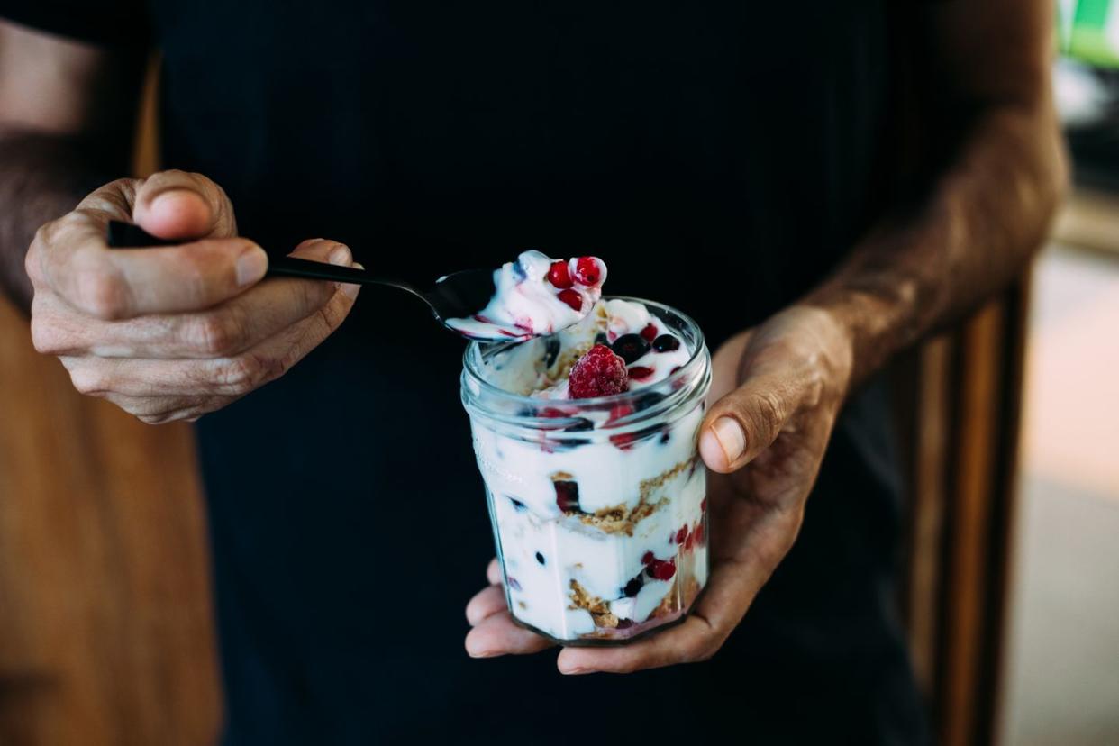 a man holding a jar of dessert made with yoghurt and frozen berry crunch