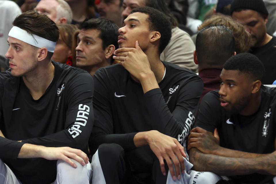 San Antonio Spurs center Victor Wembanyama, center, sits on the bench during the team's NBA basketball game against the Dallas Mavericks on Saturday, Dec. 23, 2023, in Dallas. (AP Photo/Richard W. Rodriguez)