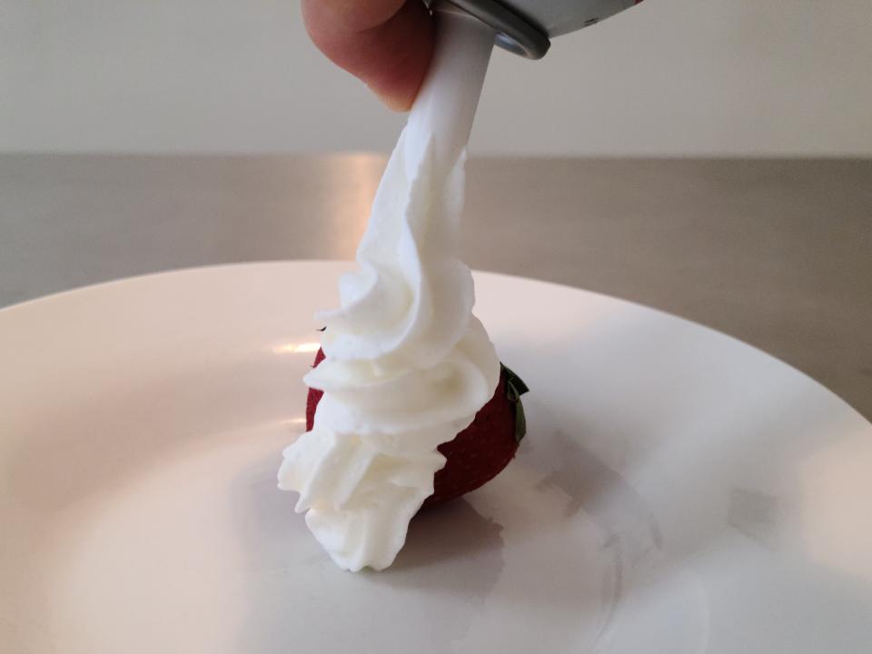 hand spraying can of cabot whipped cream onto a strawberry