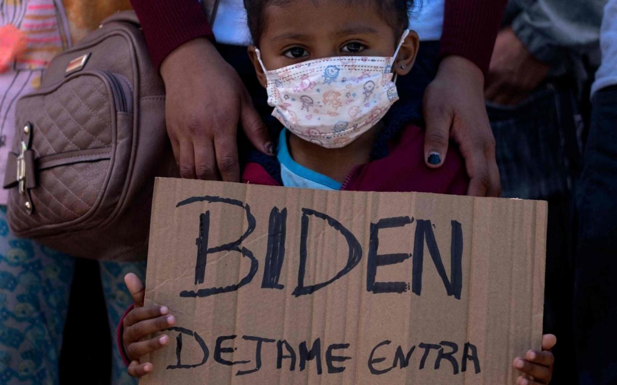 A child holds a sign which says "Biden, let me in" - Guillermo Arias / AFP