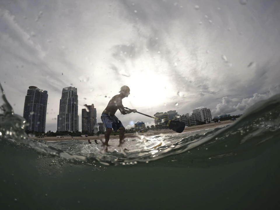 FILE - Graziano La Grasta, a local contractor and paddle board enthusiast, rides a small wave off South Beach, July 28, 2023, in Miami Beach, Fla. Across the U.S., many people are living through one of the most brutal summers of their lives and reckoning with the idea that climate change is only going to make matters worse in the coming decades. (AP Photo/Rebecca Blackwell, File)