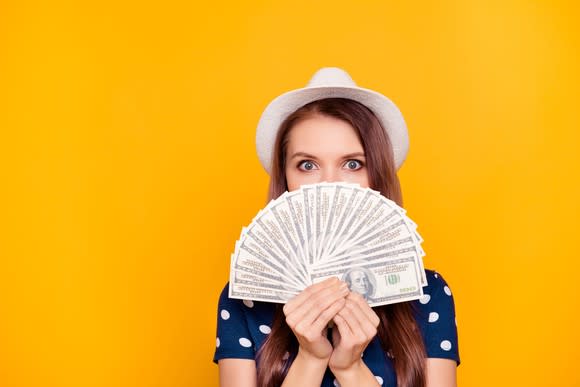 Woman holding money in front of yellow background.