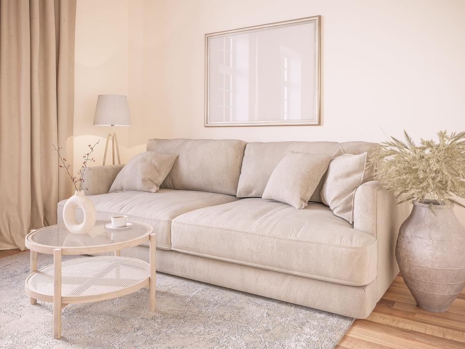 A beige living room with a light-brown couch, a boho-inspired coffee table with a vase and coffee cup on it, and a planter and lamp either side of the couch