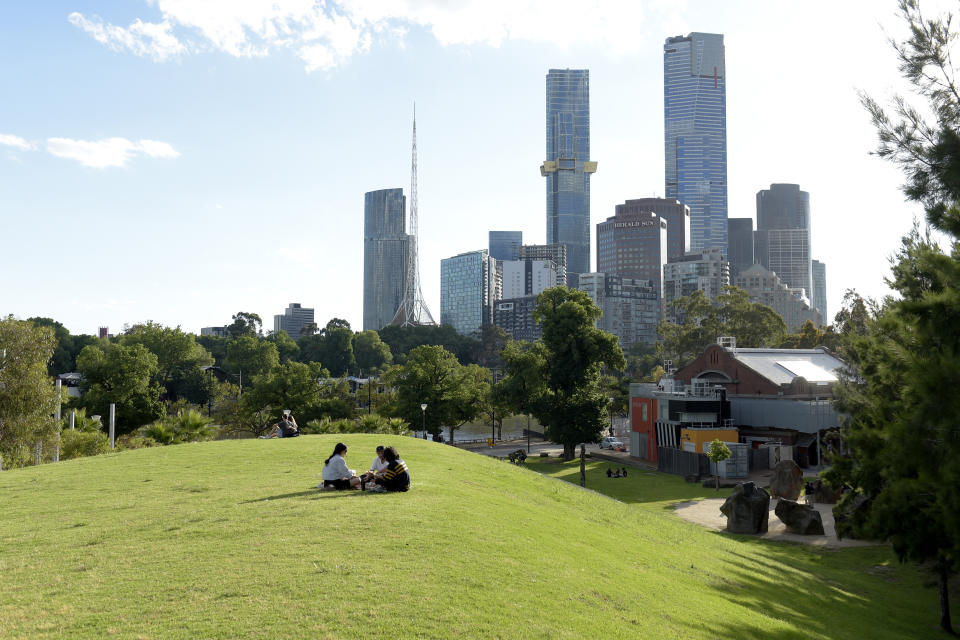 Pictured are people sitting on top of a grassy hill overlooking Melbourne's CBD.