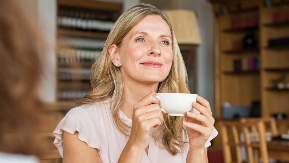 Mature woman holding coffee cup and looking away at cafeteria.