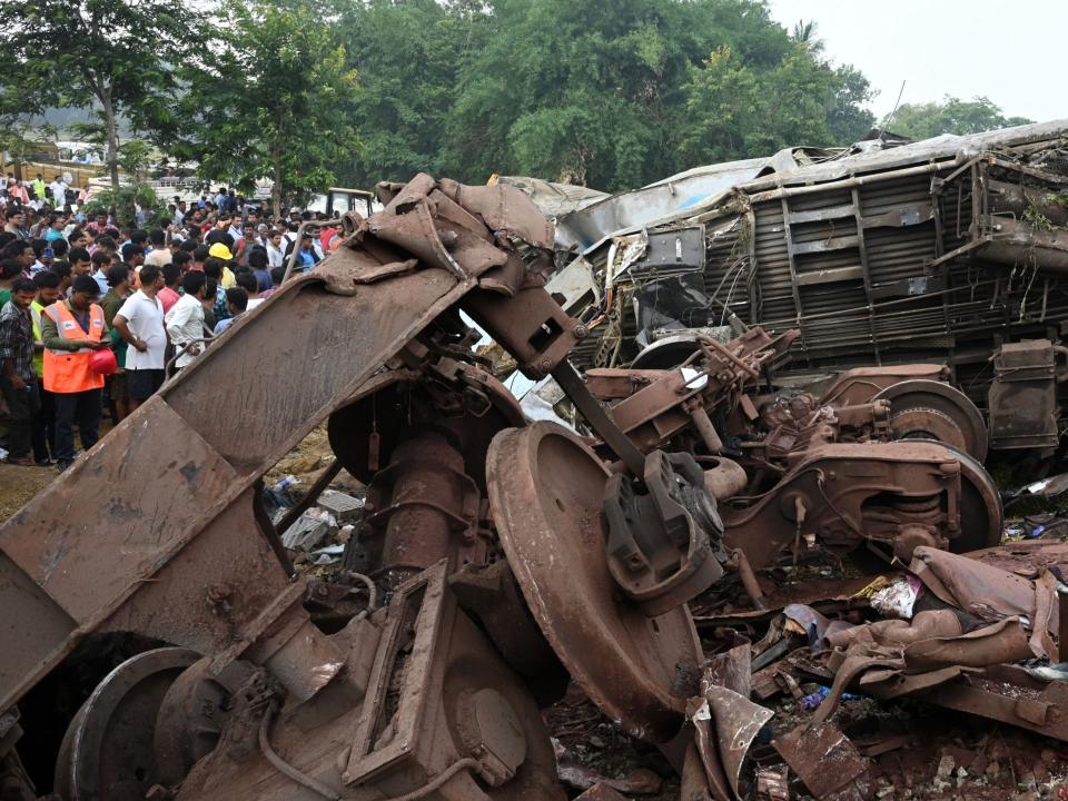 Rescue teams and onlookers gather next to wreckage at the accident site of a three-train collision near Balasore.