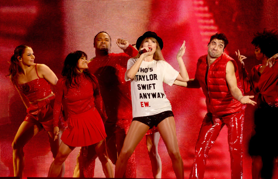 Taylor Swift sings into microphone wearing a black hat and T-shirt on stage