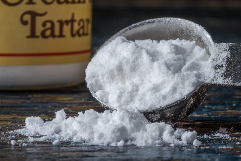 Cream of tartar spilling from a tablespoon with a cream of tartar jar in the background