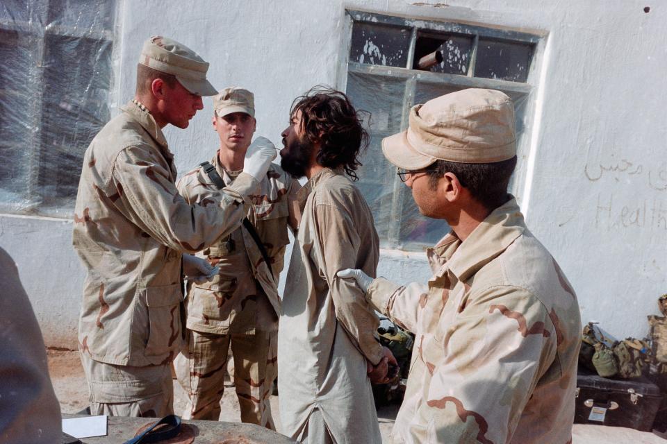 A soldier takes a mouth swab from a prisoner.