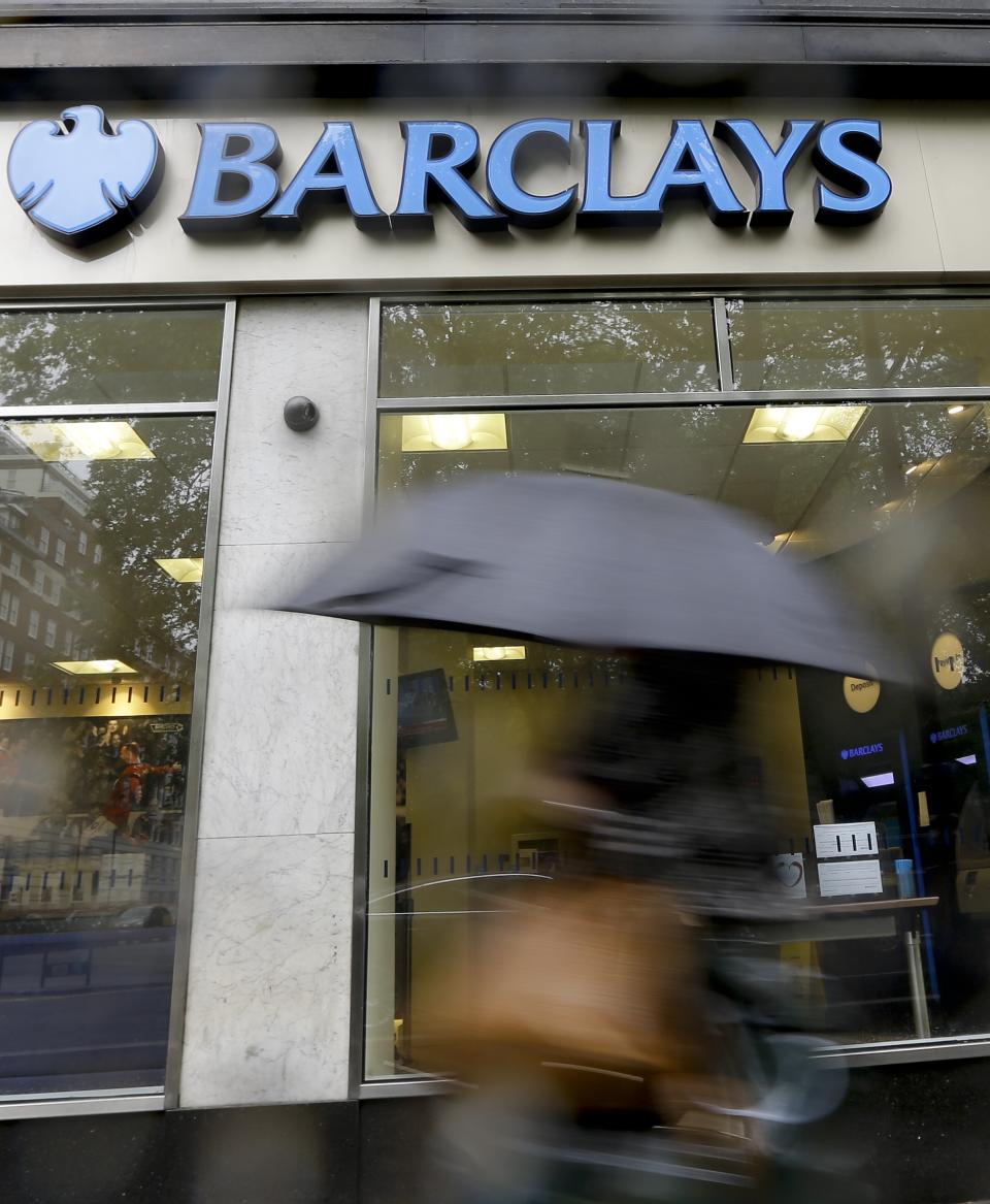 A pedestrian passes a branch of Barclays Bank in the rain in London, Thursday, May 8, 2014. British bank Barclays says it will cut around 14,000 jobs this year as it looks to streamline its operations and reduce the size of its investment banking arm. The figure was higher than anticipated — previously the bank had indicated that it was looking to get rid of between 10,000 and 12,000 people. (AP Photo/Kirsty Wigglesworth)