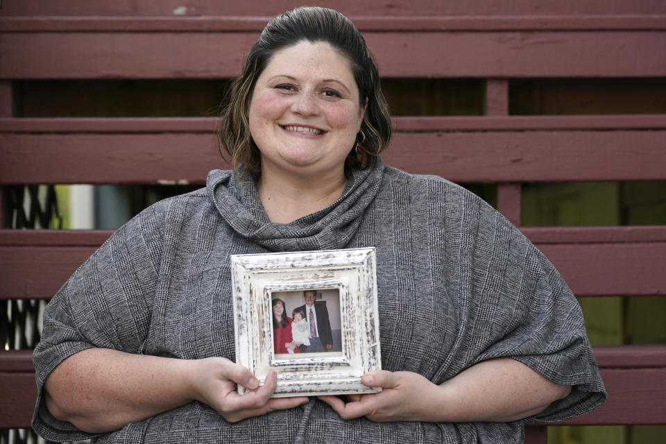 Caitlin Joyce holds a photo of herself as a child held by her parents as she poses for a photo at her home Saturday, Aug. 29, 2020, in Edmonds, Wash. Joyce's family is forging ahead with a Thanksgiving holiday feast in Virginia and she plans to join them. They plan to set up plywood tables on sawhorses in a large garage so they can sit six feet apart where "It will be almost like camping." (AP Photo/Elaine Thompson)